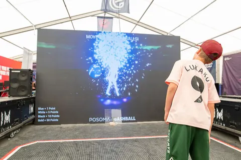 Kind spielt Bashball, sein Körper erscheint als leuchtende Partikelfigur auf der LED-Wand