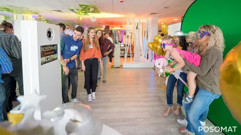 Gäste posieren mit Requisiten vor einem Greenscreen, daneben die Fotobox