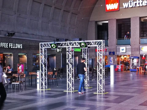 Torbögen aus Traversen mit Displays in einer Bahnhofshalle, Passanten gehen hindurch